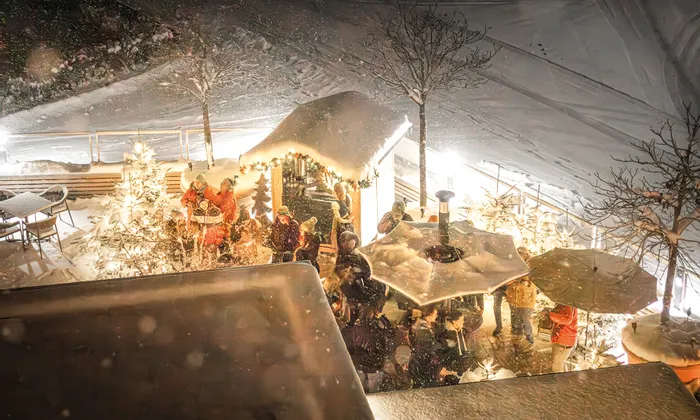 Menschenmenge genießt gemütlichen Weihnachtsmarkt in verschneiter Winternacht mit Lichtern und Dekorationen